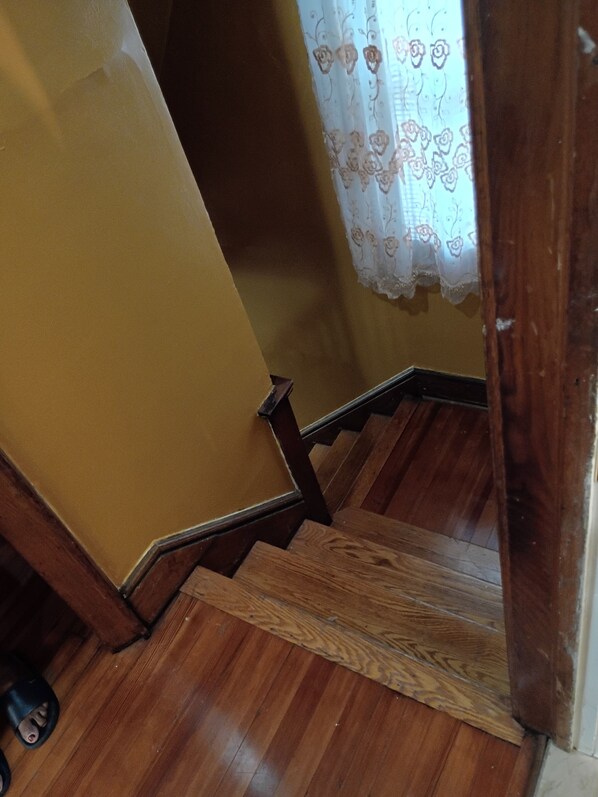 Eine Holztreppe mit Handlauf, die zu einem Raum mit gelber Wand und einem blumigen Vorhang führt.