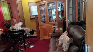 Un salon avec une moquette rouge, un canapé en cuir marron, une table à manger avec des chaises et un buffet en bois doté de portes en verre.