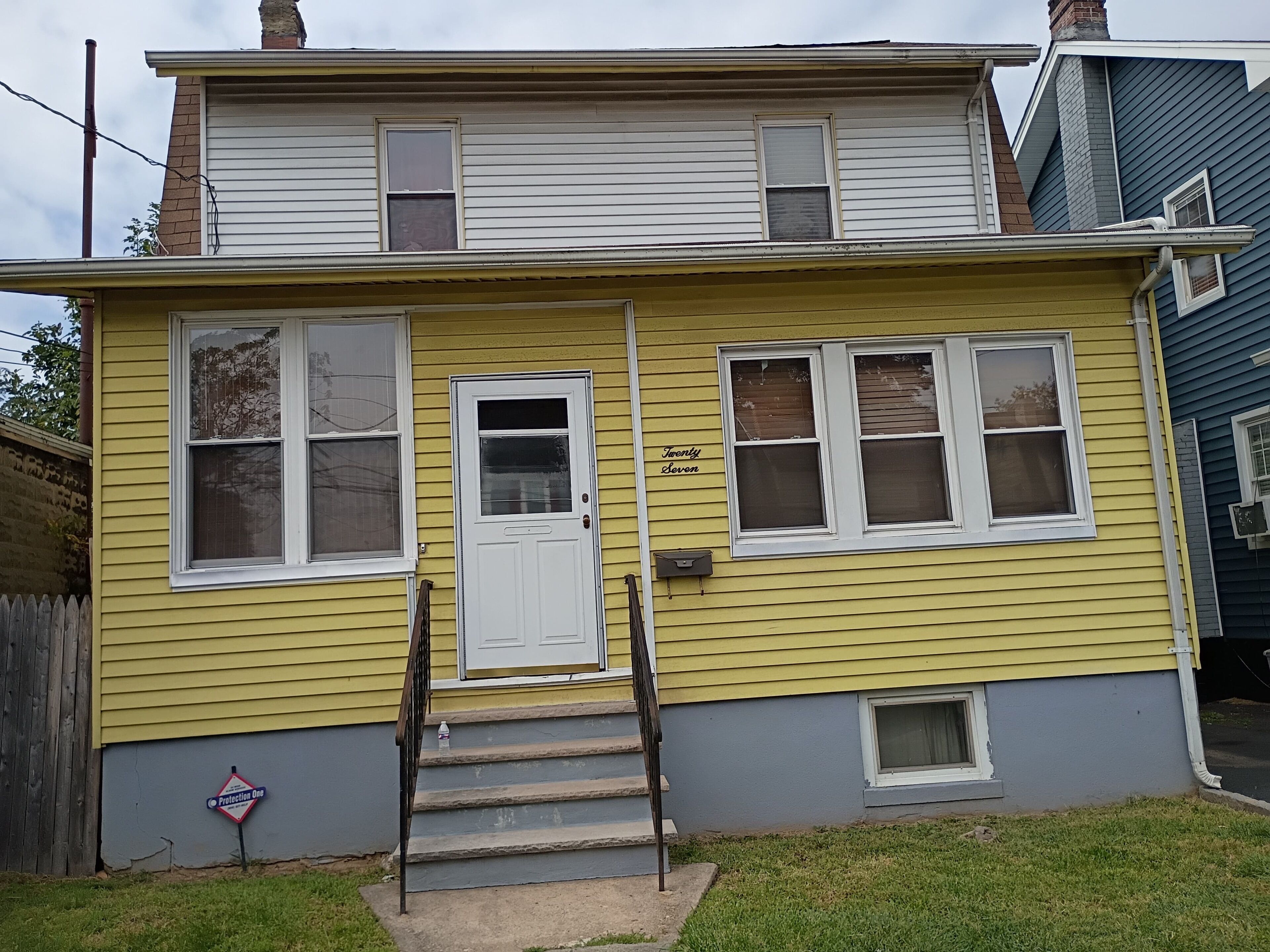 A two-story house with a front door, a small set of steps, and a mailbox.
