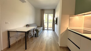A modern kitchen with a built-in stove, a dining area with a table and chairs, and a sliding glass door leading to a balcony. - Modern Flat in Central Bibione (San Michele al Tagliamento)
