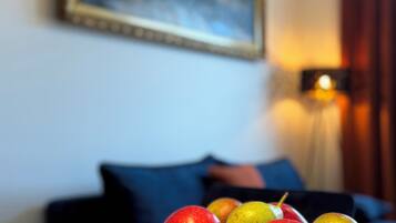 A wooden bowl with apples on a table in a room with a painting on the wall and a lamp in the background.
