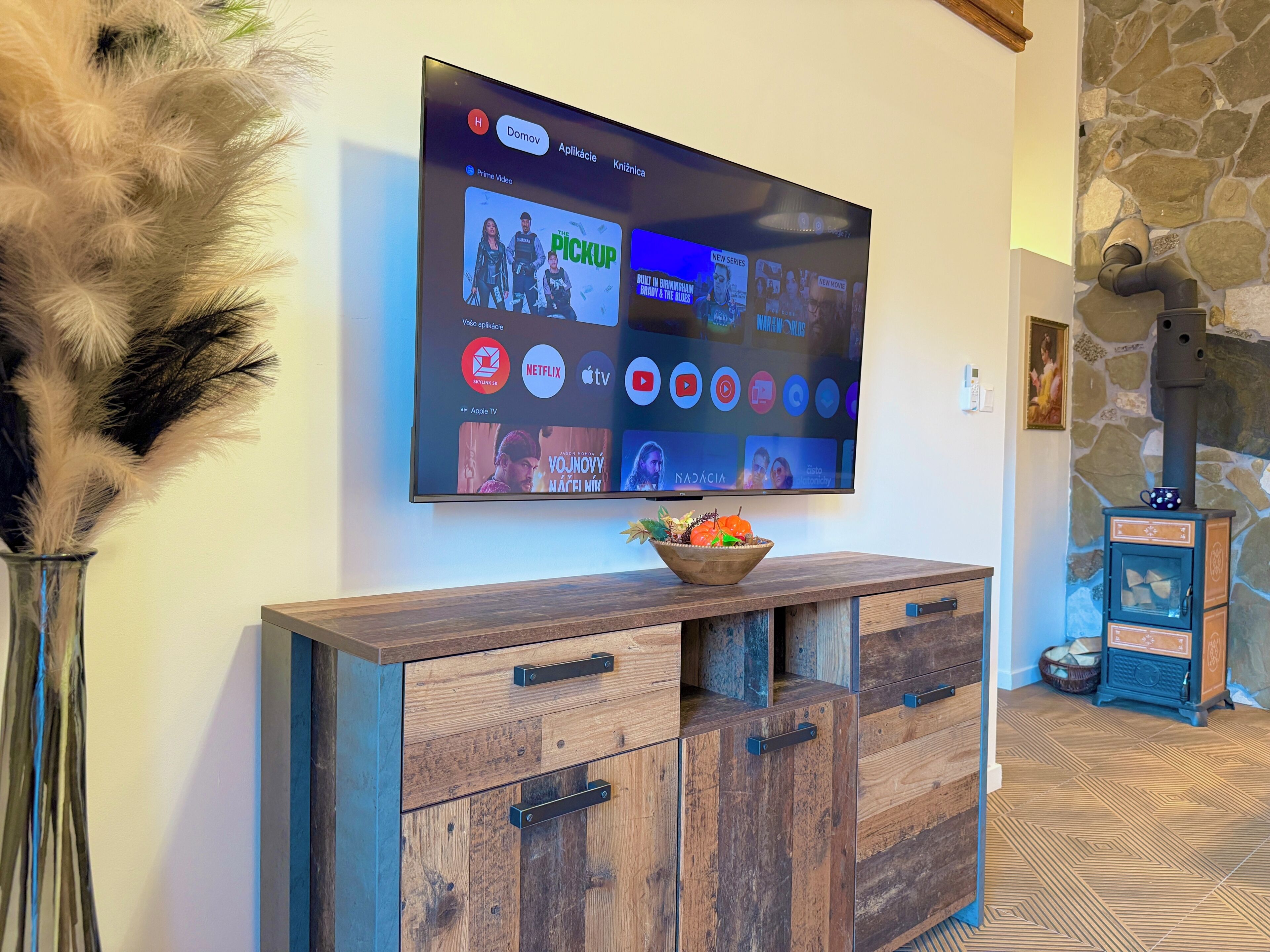 Ein flachbildfernseher an der Wand, der verschiedene Streaming-Dienste anzeigt, und ein Holzkonsolentisch mit einer dekorativen Schale.
