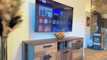 Ein flachbildfernseher an der Wand, der verschiedene Streaming-Dienste anzeigt, und ein Holzkonsolentisch mit einer dekorativen Schale.