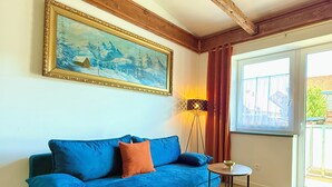 A blue sofa with a pink rug, a small round table, a lamp, and a painting on the wall. - Residence S5 - Comfort Living Apartment  (Prešov)
