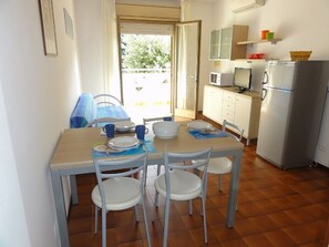 A small, bright kitchen with a dining table set for four, white chairs, and a refrigerator. - Great Flat in Bibione-beahost (San Michele al Tagliamento)