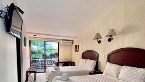 Habitación de hotel con dos camas, un televisor montado en la pared y vistas al exterior a través de una puerta corrediza de vidrio.