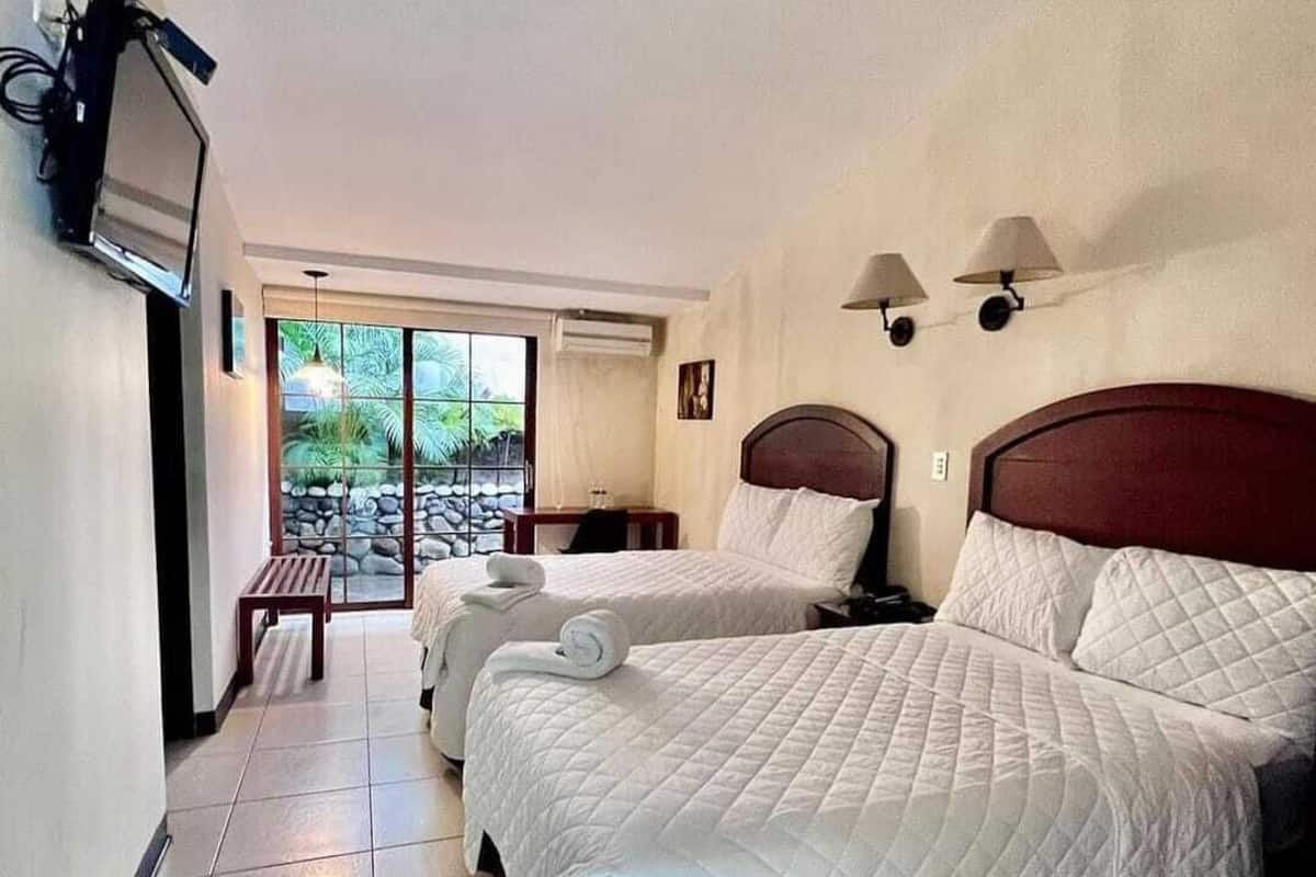 Habitación de hotel con dos camas, un televisor montado en la pared y vistas al exterior a través de una puerta corrediza de vidrio.