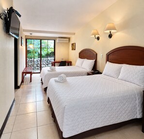 Une chambre d’hôtel avec deux lits, un bureau, une chaise, un téléviseur fixé au mur et une vue sur la verdure par la fenêtre.