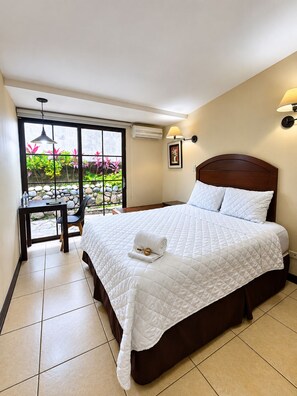Une chambre d’hôtel avec un lit, un bureau et une vue sur un jardin, accessible par une porte coulissante.