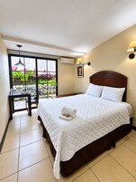 A hotel room with a bed, a desk, and a view of a garden through a sliding door.