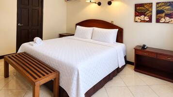 Habitación de hotel con cama, mesita de noche, banco, aire acondicionado de pared, apliques y obras de arte.