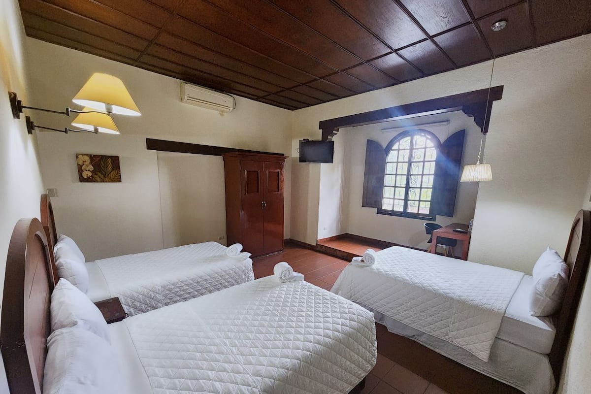 Una habitación con dos camas, un armario de madera, una mesita y una ventana con vistas.