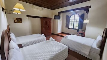 A room with two beds, a wooden wardrobe, a small table, and a window with a view.