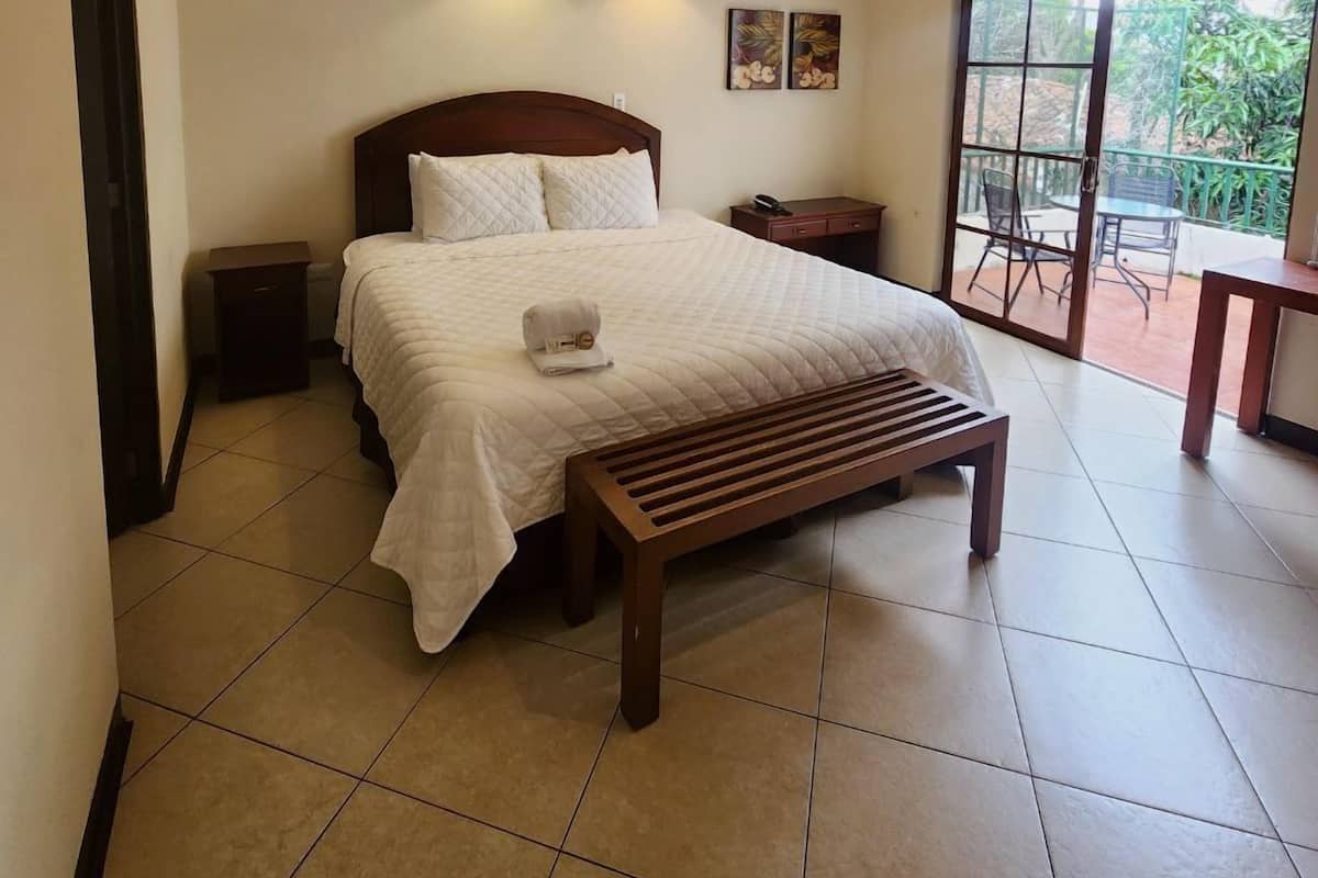 Un dormitorio con cama, mesitas de noche, aire acondicionado, lámparas fijadas a la pared y vistas al exterior a través de un ventanal corredera.