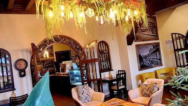 Un interior acogedor con vigas de madera, una lámpara de planta colgante y una zona de estar con sillas y una mesa.