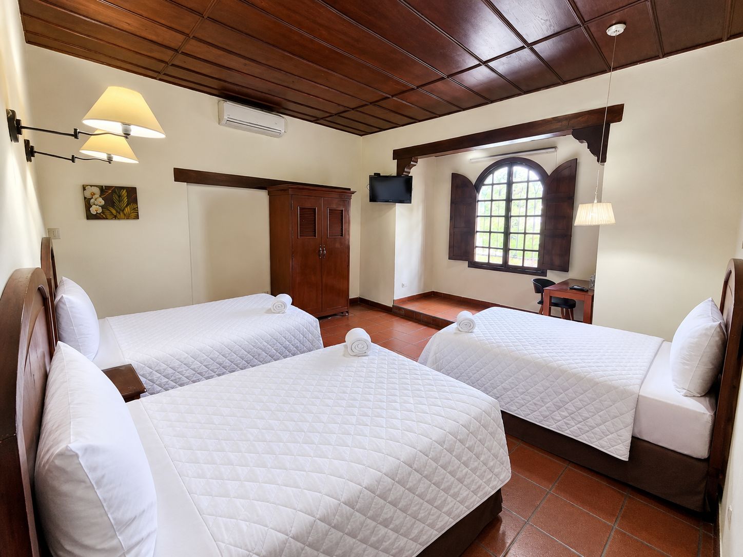 Habitación de hotel con dos camas, un armario de madera, un escritorio, una silla, un televisor y una ventana con vistas.