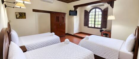 Habitación de hotel con dos camas, un armario de madera, un escritorio, una silla, un televisor y una ventana con vistas.