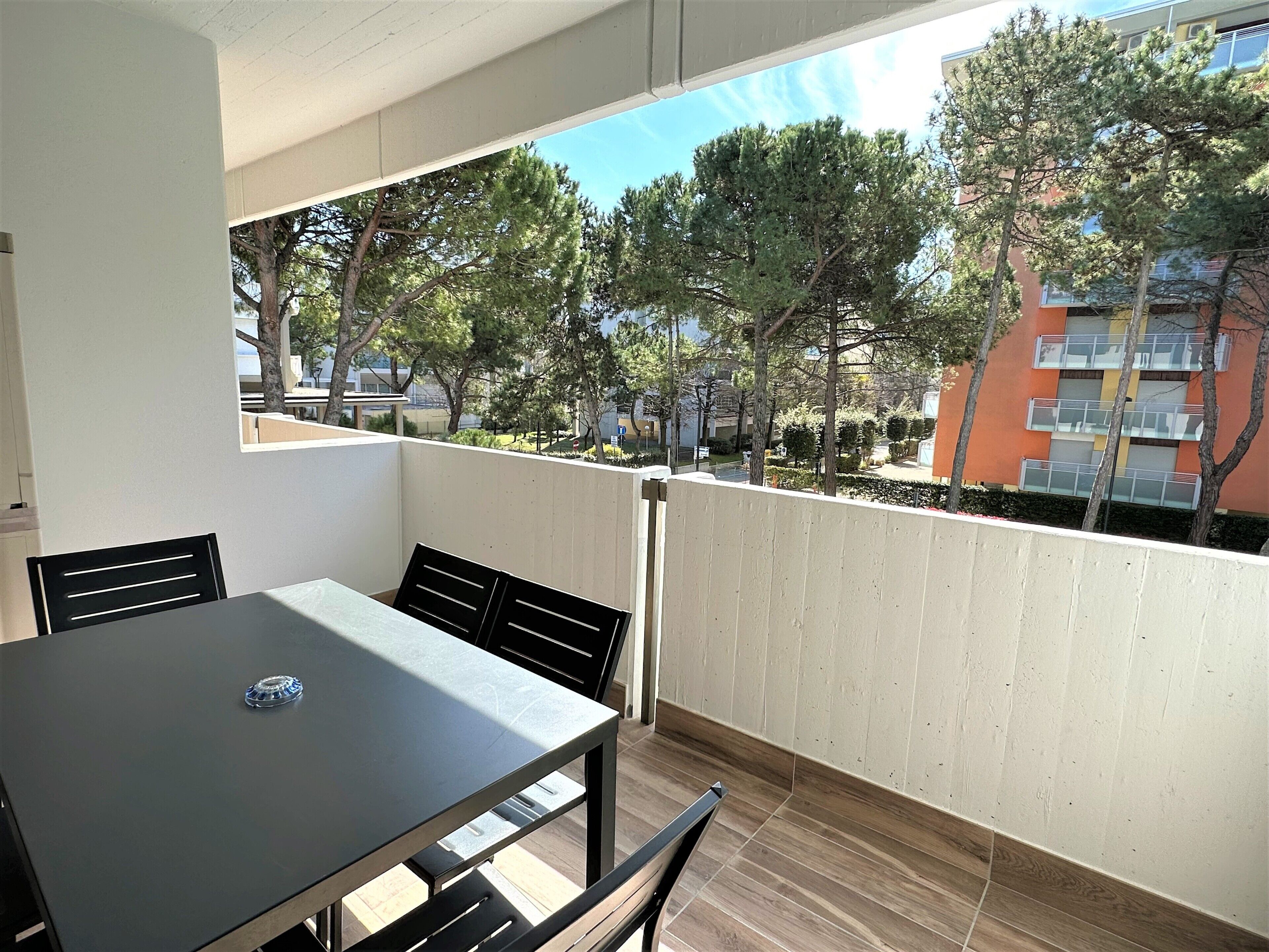 Ein Balkon mit Tisch und Stühlen, der auf ein Wohngebiet mit Bäumen und Gebäuden blickt.