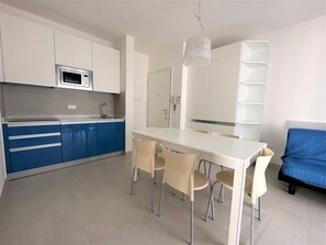 A modern kitchen with white and blue cabinets, a microwave, and a dining area with a white table and four chairs.