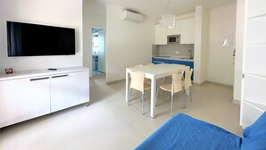 Una sala moderna con un televisor de pantalla plana, un comedor con mesa y sillas, y una kitchenette con microondas.