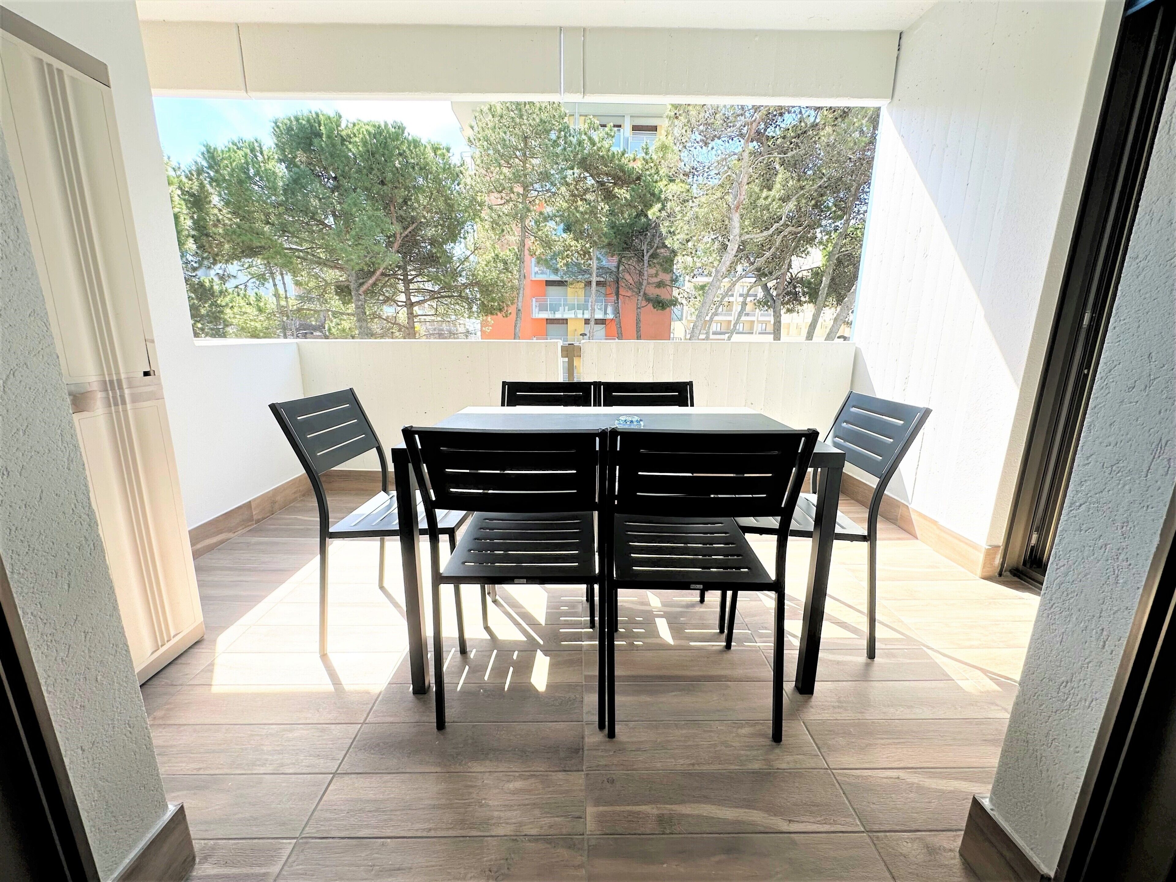 A balcony with a table and chairs, a view of trees and buildings, and a tiled floor.