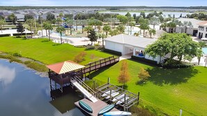 Un muelle a orillas del río con kayaks, una zona de estar cubierta y un edificio de fachada blanca.
