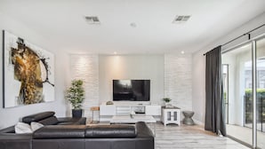 Una sala moderna con un sofá grande de cuero negro, un televisor de pantalla plana, una mesa de centro blanca y un muro con diseño.