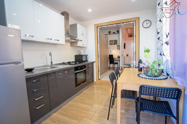 Una cocina moderna con horno integrado, microondas y cocina a gas. Hay una zona de comedor con mesa y sillas de madera.