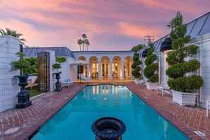 A swimming pool with a fountain, surrounded by a brick patio and white walls.