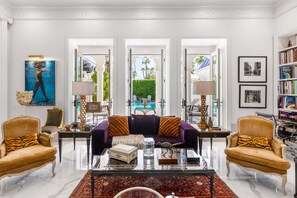 A spacious living room with a purple sofa, two armchairs, a coffee table, and a bookshelf.
