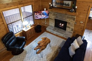 A cozy cabin interior with a stone fireplace, leather recliner, and a flat-screen TV mounted on the wall. - Stay three & Play for free (Sevierville)