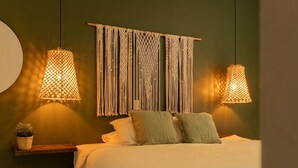 Una camera da letto con un letto, due lampade appese in macramè, un arazzo da parete in macramè e una piccola pianta in vaso su uno scaffale.