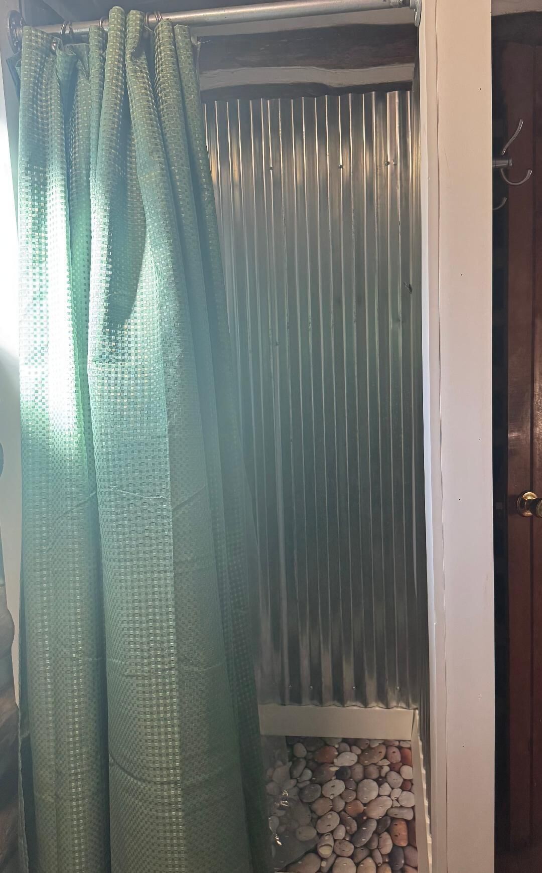 A room with a green curtain, a metal vent, and a shelf with pebbles.