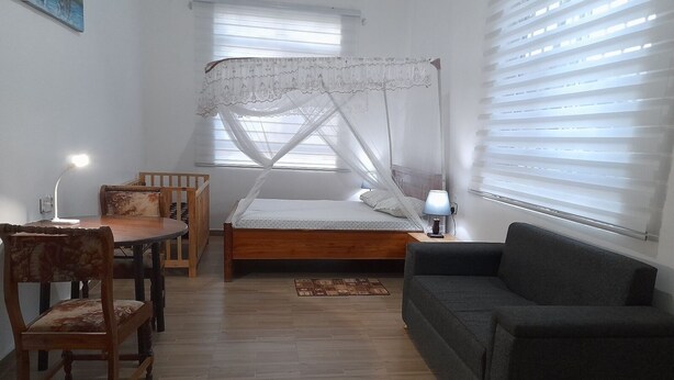Ein Schlafzimmer mit einem Bett, einem Schreibtisch, einem Sessel, einer Couch und einem Fenster mit Jalousien.