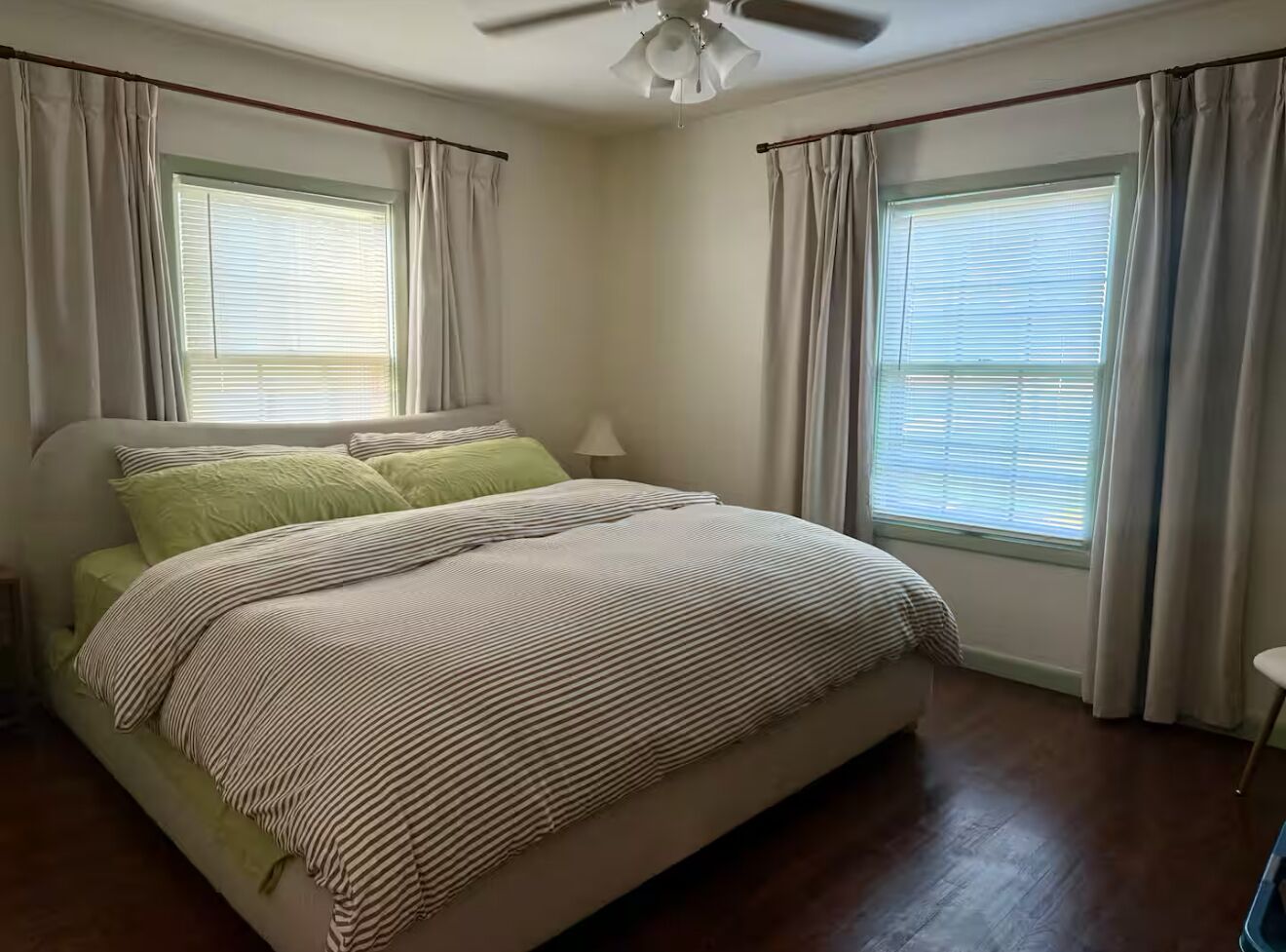 Un dormitorio con cama, cortinas, ventilador de techo y ventanas.