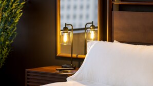 A hotel room with a bed, a nightstand, a mirror, and a view of a building through the window.