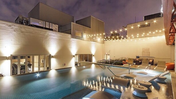 A pool area with lounge chairs, a water feature, and string lights.