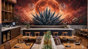A restaurant with a mural of a moon and cactus, wooden tables, and a bar area.