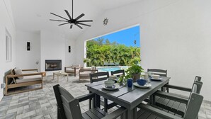 Ein moderner Essbereich im Freien mit Blick auf einen Pool, einem Deckenventilator und einem Kamin.