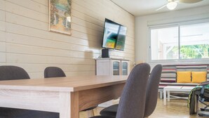 Un comedor con mesa y sillas de madera, un televisor sobre un mueble bajo y un sofá con cojines.