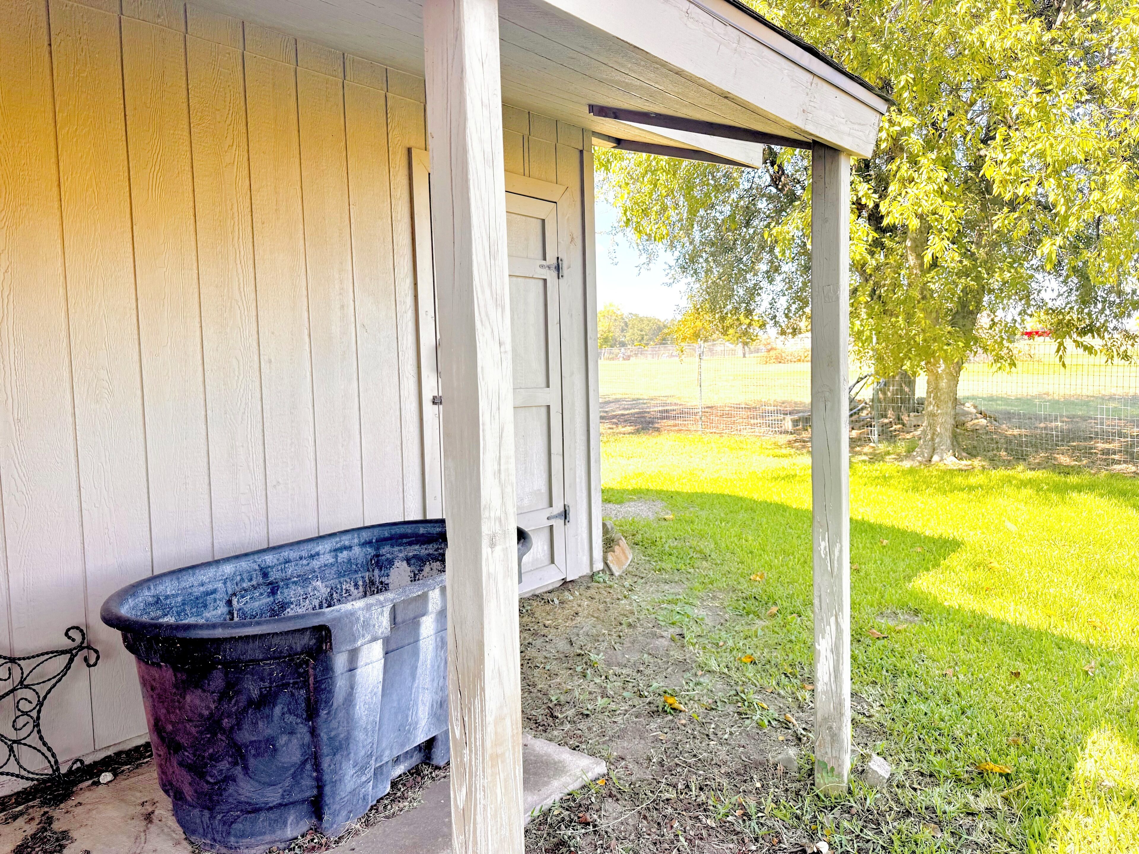 A covered porch with a wooden wall, a concrete planter, and a grassy yard with trees.