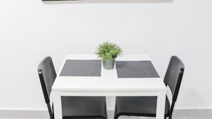 Ein weißer Esstisch mit schwarzen Stühlen, ein Blumentopf und ein großes abstraktes Gemälde an der Wand.