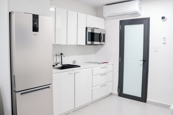 Een moderne keuken met witte kasten, een ingebouwde magnetron en een koelkast.