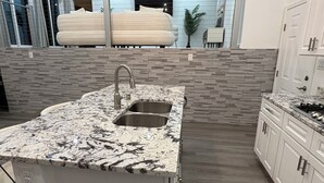 A modern kitchen with a granite countertop, stainless steel sink, and white cabinetry. - Palisades hills home with City Mountain View’s  (Albuquerque)