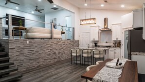 A modern kitchen with a stone backsplash, white cabinets, and a dining area with a wooden table and bar stools. - Palisades hills home with City Mountain View’s  (Albuquerque)