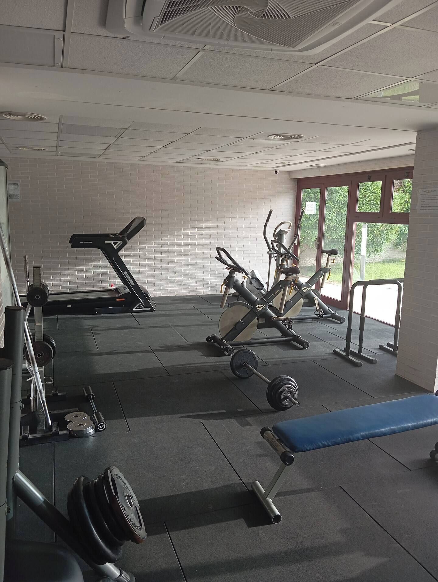 Ein Fitnessraum mit Trainingsgeräten, Laufband, Ergometer und einer Bank.