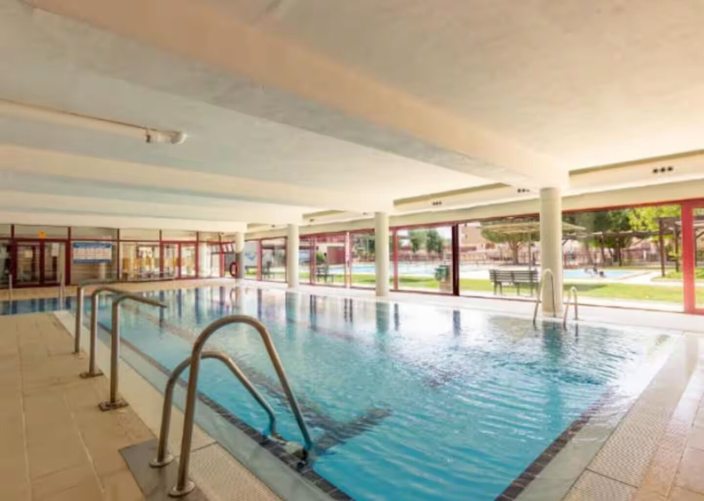 An indoor swimming pool with clear water, surrounded by glass walls and a tiled floor.