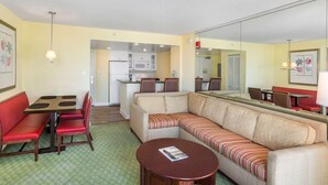 Een hotelkamer met een zithoek, een bank, een ronde tafel en een keuken op de achtergrond.