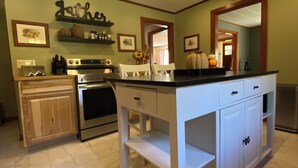 A kitchen with white cabinets, a black countertop, and a stove. There are framed pictures on the wall and a shelf with bottles.