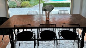 A dining area with a wooden table and metal chairs, a vase with flowers, and a view of a swimming pool through a glass door.